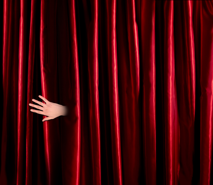 hand emerging from behind red theatre curtain